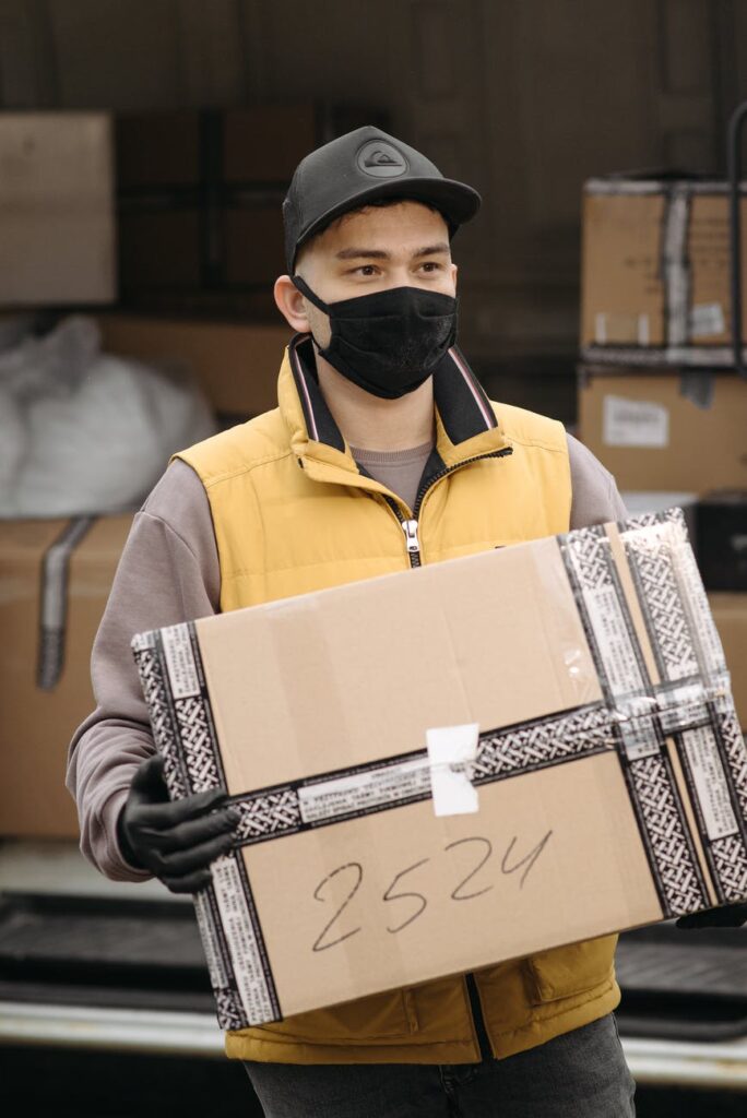 man wearing face mask carrying brown carton box