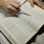 a close up shot of a person holding a pen and an open book
