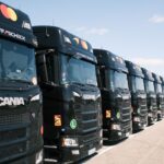 long line of black scania trucks in a row outdoors